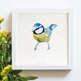 A watercolour painting of a Blue Tit (Cyanistes caeruleus). The blue and yellow bird rests on branches and twigs. The painting is in a white wooden frame which is placed on a white background. Next to the bird is bunch of yellow flowers.