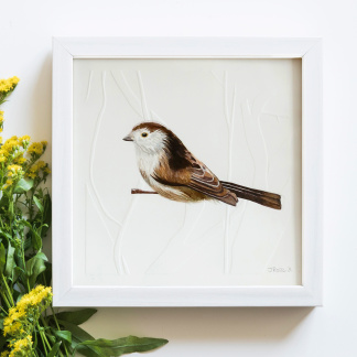 A watercolour painting of a Long Tailed Tit (Aegithalos caudatus). The brown & white bird grasps onto blind embossed branches. The painting is in a white wooden frame which is placed on a white background. Next to the bird is bunch of yellow flowers.